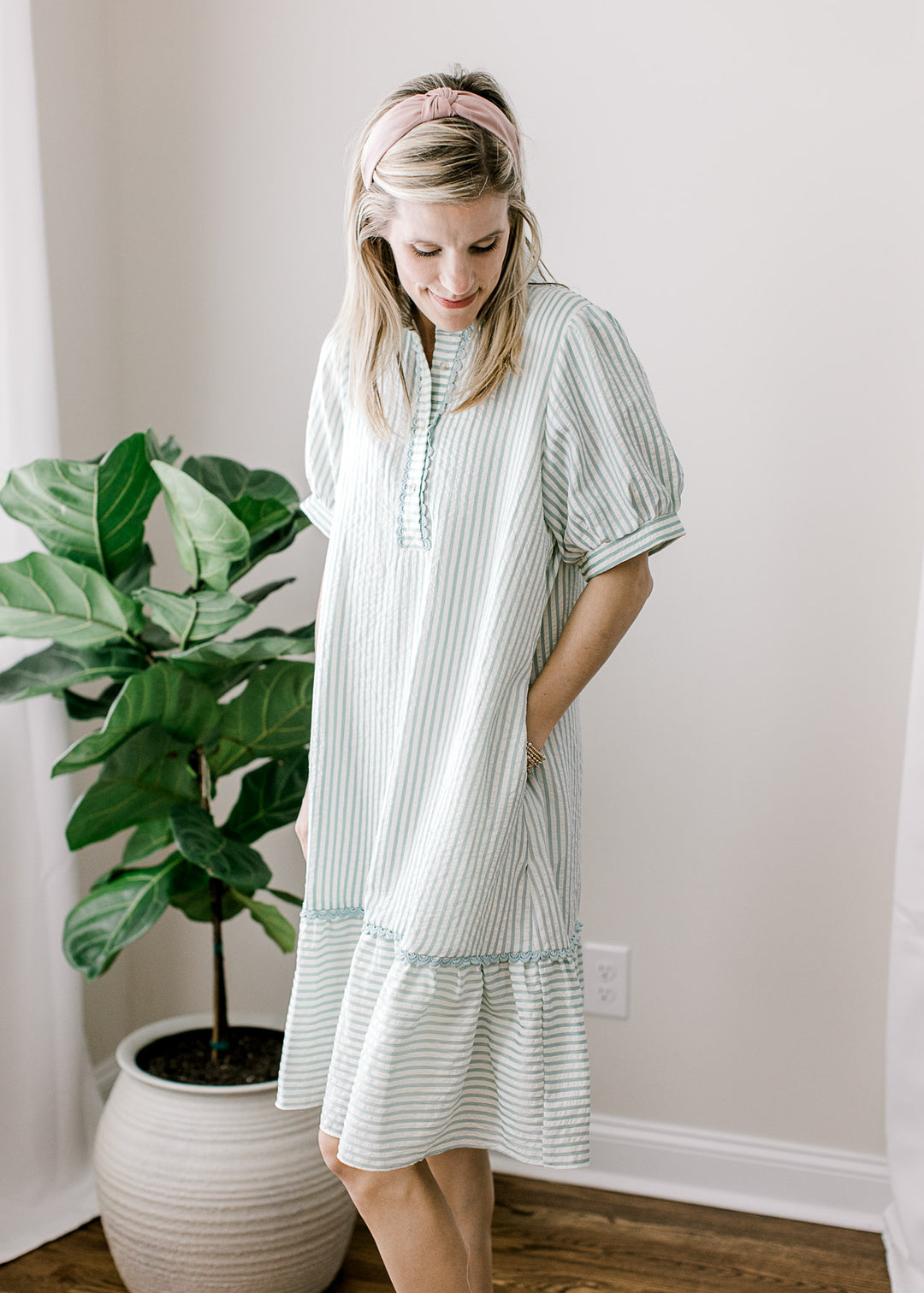 Model wearing a sage blue and cream stripe dress with scalloped trim at the neck, collar, and hem.