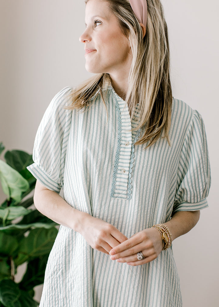 Model wearing a sage blue and cream stripe dress with short sleeves, v-neck and a button placket.
