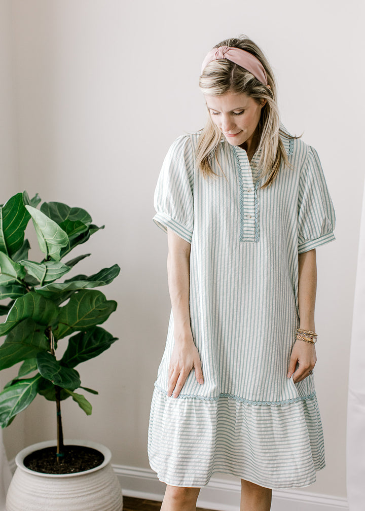 Model wearing a sage blue and cream stripe above the knee dress with short sleeves. 
