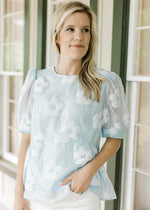 Model wearing a light blue top with stitched flowers and sheer bubble short sleeves.