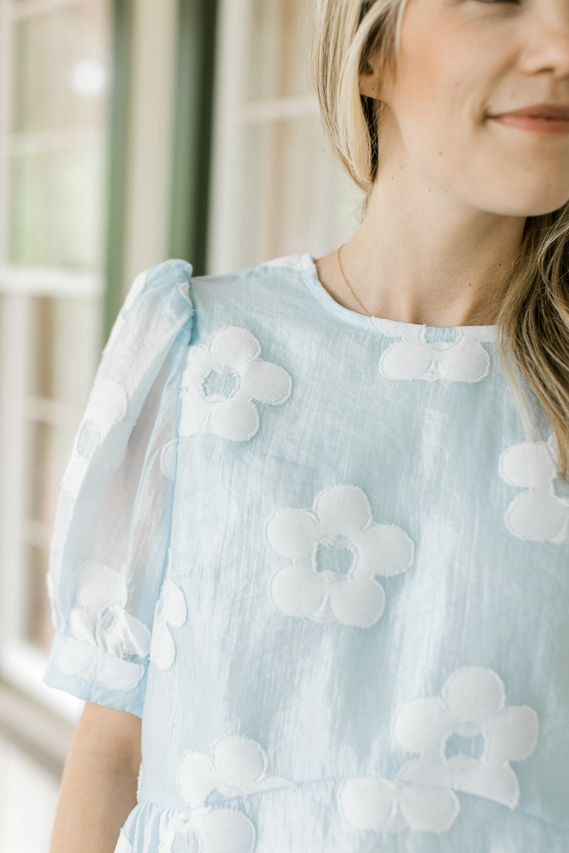 Close up of sheer bubble short sleeves, on a light blue babydoll top with stitched flowers. 