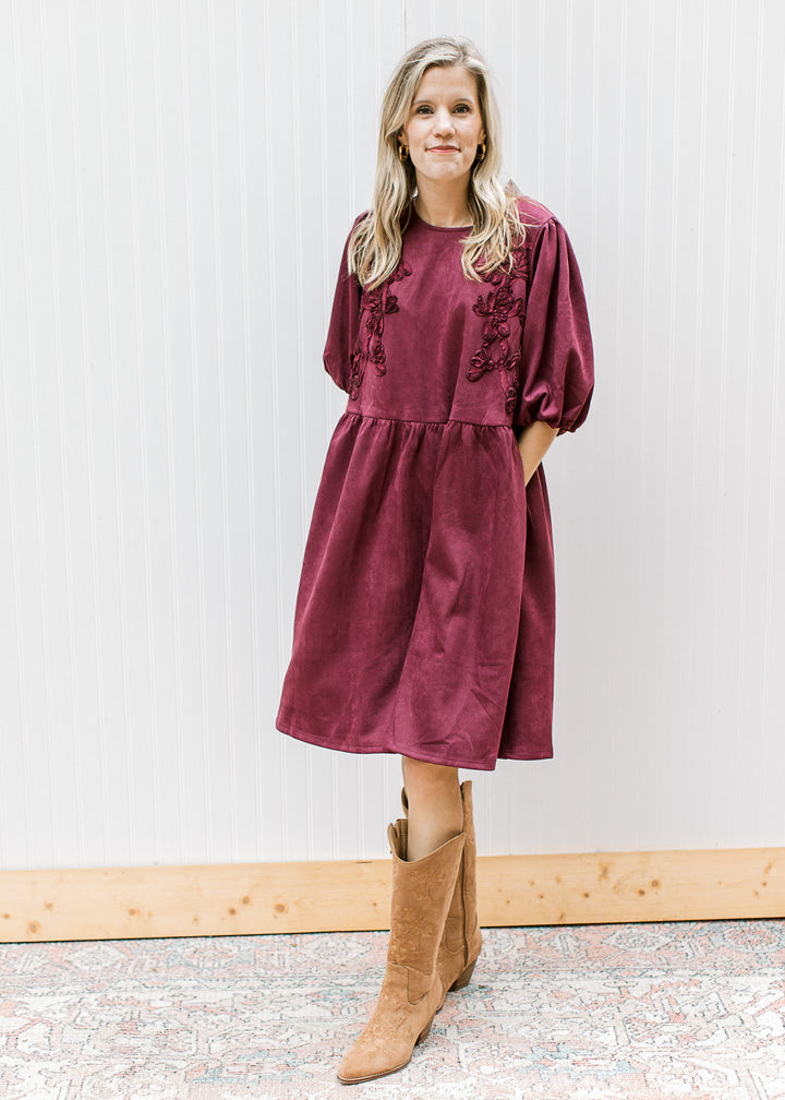 Model wearing boots and a suede burgundy dress with subtle floral detail and bubble sleeves.
