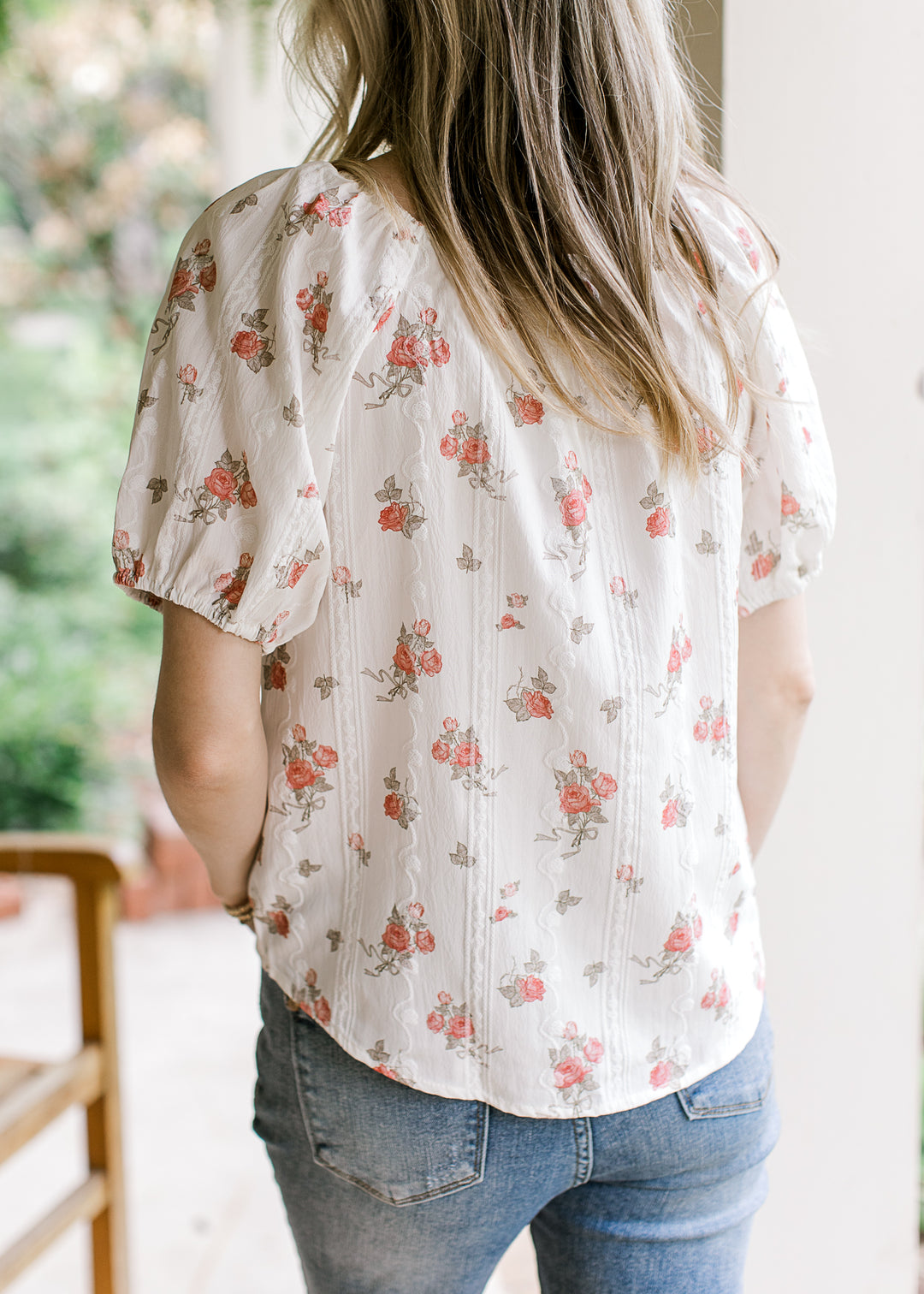 Back view of Model wearing a white top with pink roses and short sleeves with elastic.