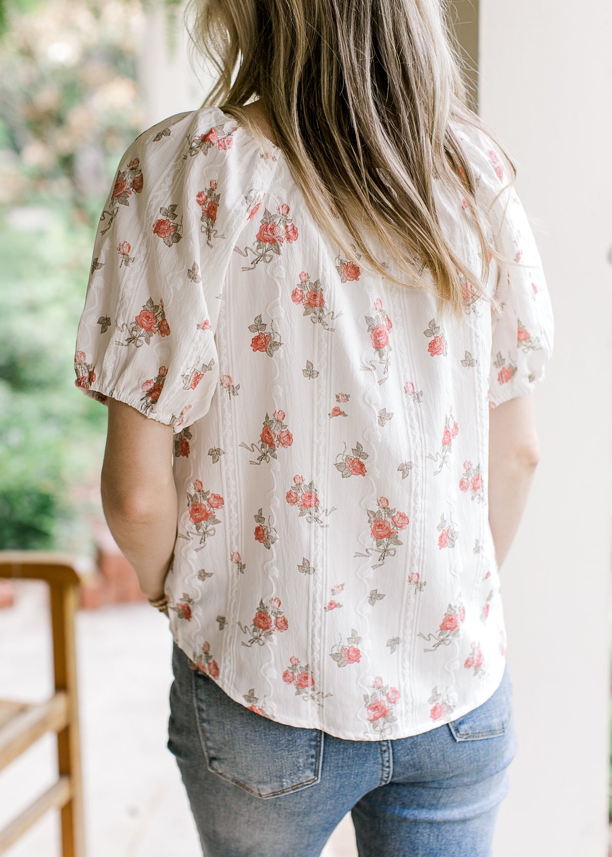 Back view of Model wearing a white top with pink roses and short sleeves with elastic.