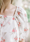 Close up of buttons and square neck on a white top with pink roses and bubble short sleeves. 