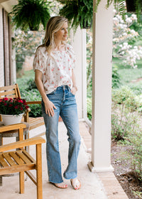 Model wearing jeans and a white square neck top with pink roses, short sleeves and buttons.