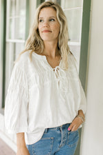 Model wearing a cotton white top with 3/4 sleeves and a v-neck with ties. 