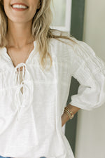 Close up of two ties on the v-neck of a white cotton top with 3/4 sleeves. 