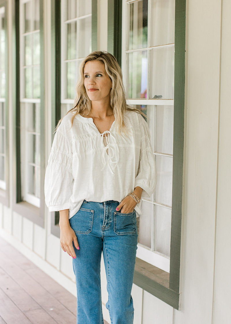 Model wearing a cotton white top with 3/4 bubble sleeves and a v-neck with ties.