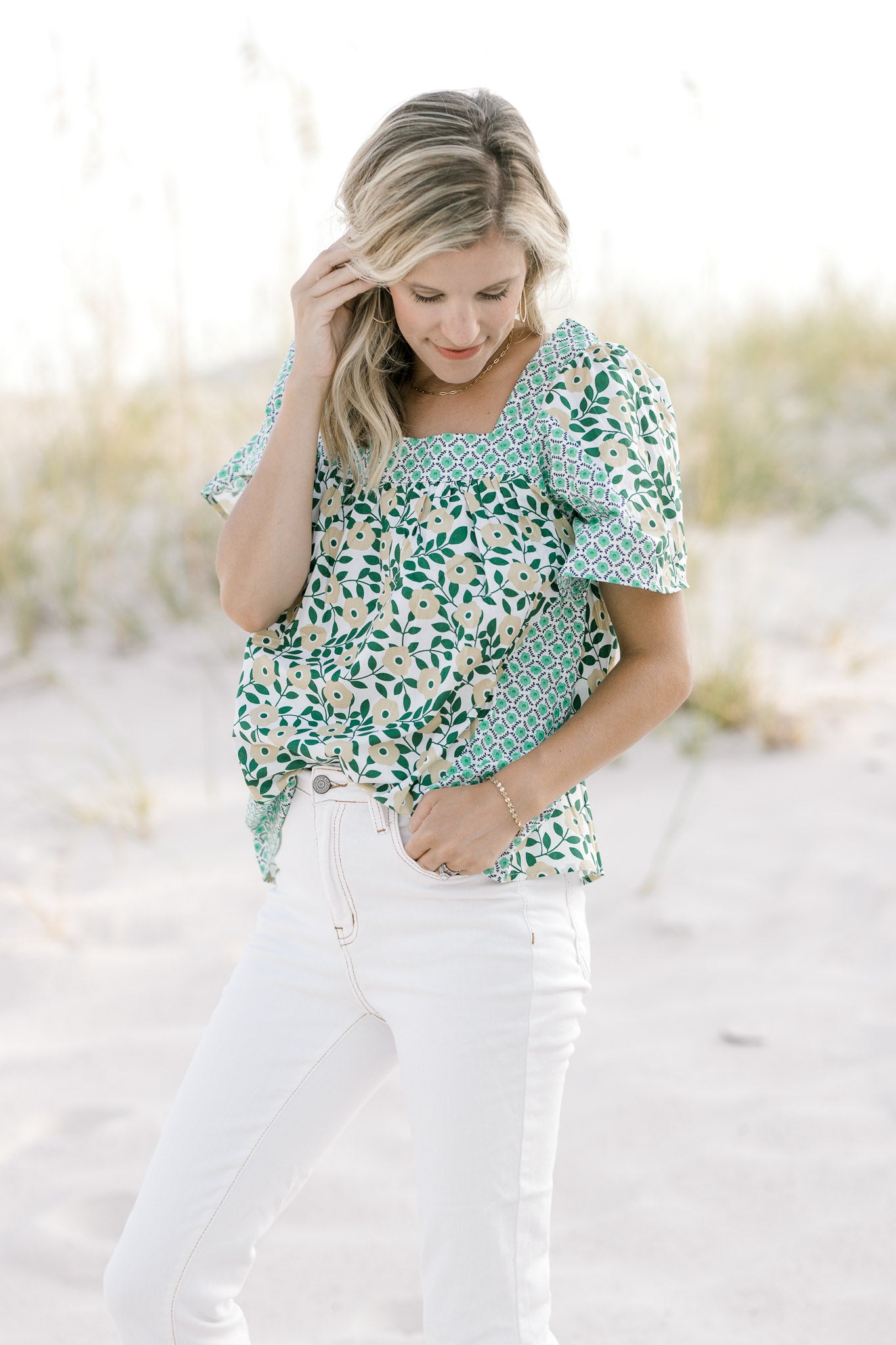 Model wearing a mixed green floral pattern top with a square neckline tucked into white pants.