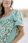 Close up view of square neck and short sleeves on a mixed green floral top. 