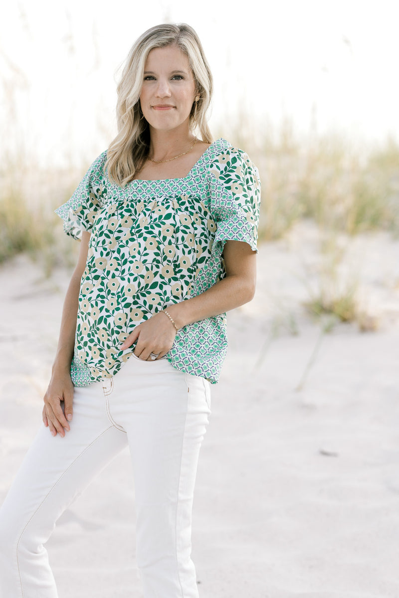 Model wearing white jeans and a mixed green floral pattern top with a square neck and short sleeves.