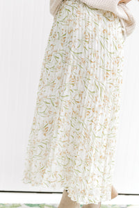 Model wearing a white maxi skirt with a cream floral pattern that is pleated with an elastic waist. 
