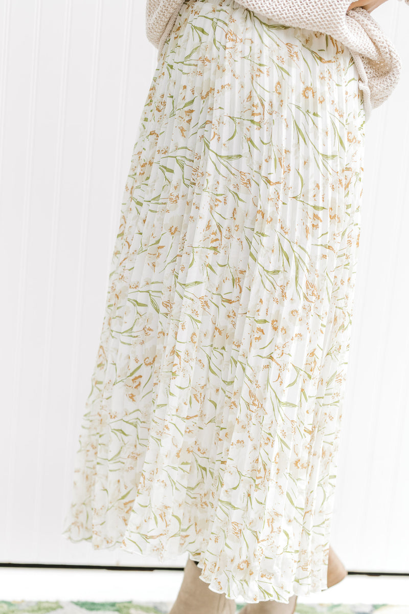 Model wearing a white maxi skirt with a cream floral pattern that is pleated with an elastic waist. 
