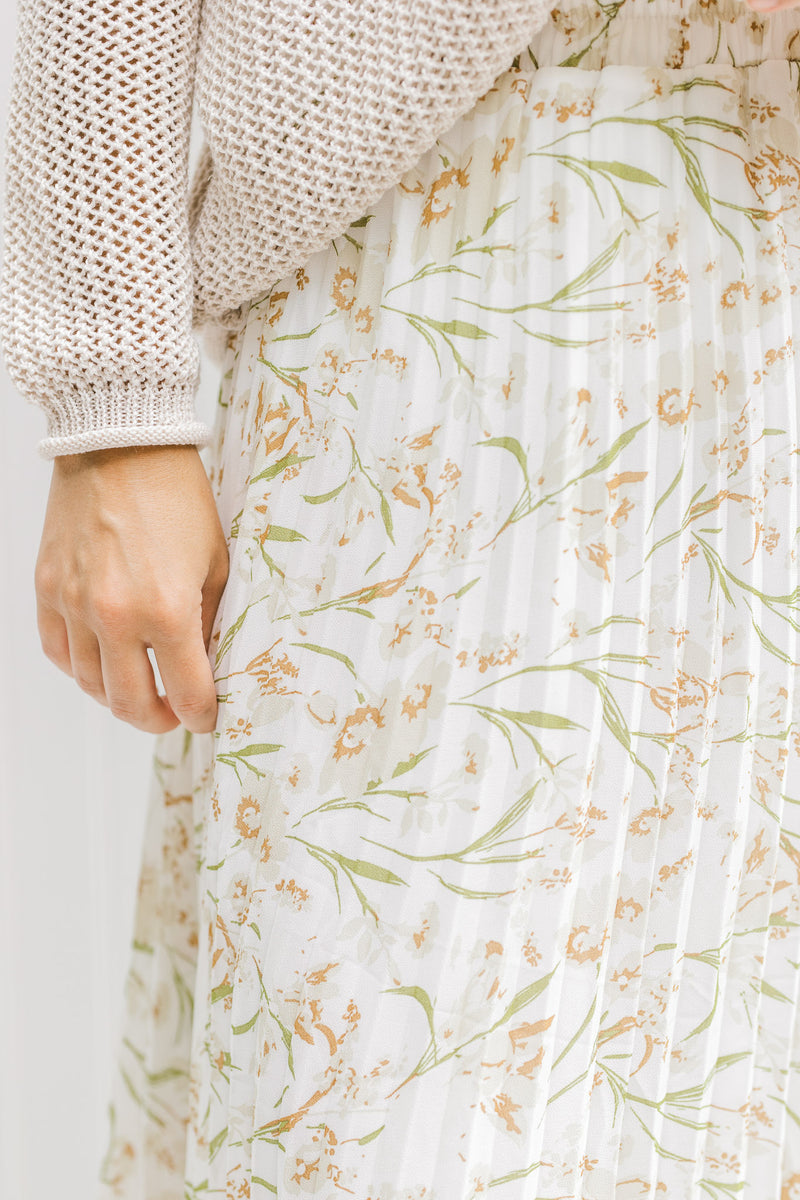 Close up view of model wearing a white pleated maxi skirt with a cream floral pattern.