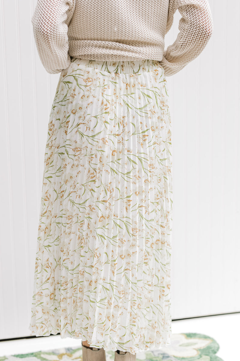 Back view of Model wearing a white maxi skirt with a cream floral pattern and an elastic waistband. 