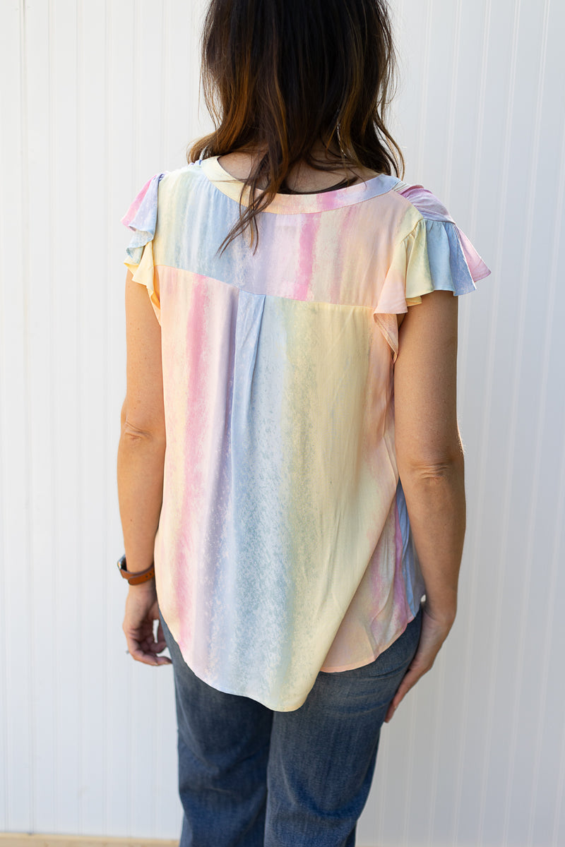 Back view of Model wearing a bright ombre top with a v-neck and flutter cap sleeves.