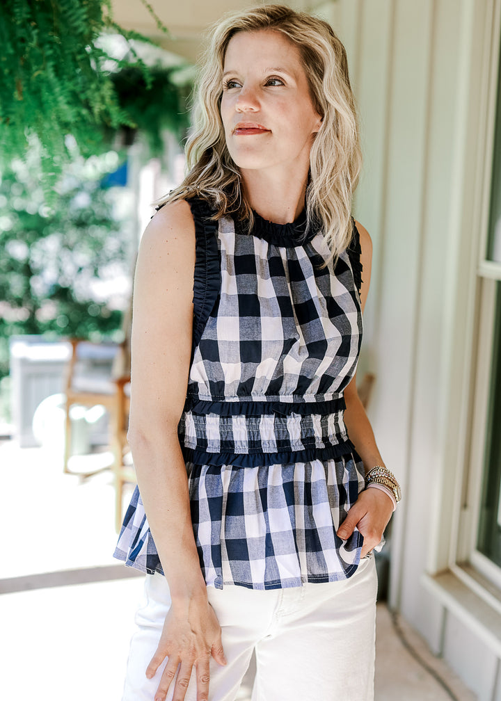 Model wearing a navy and white gingham sleeveless top with a navy ruched detail at neck and arm.