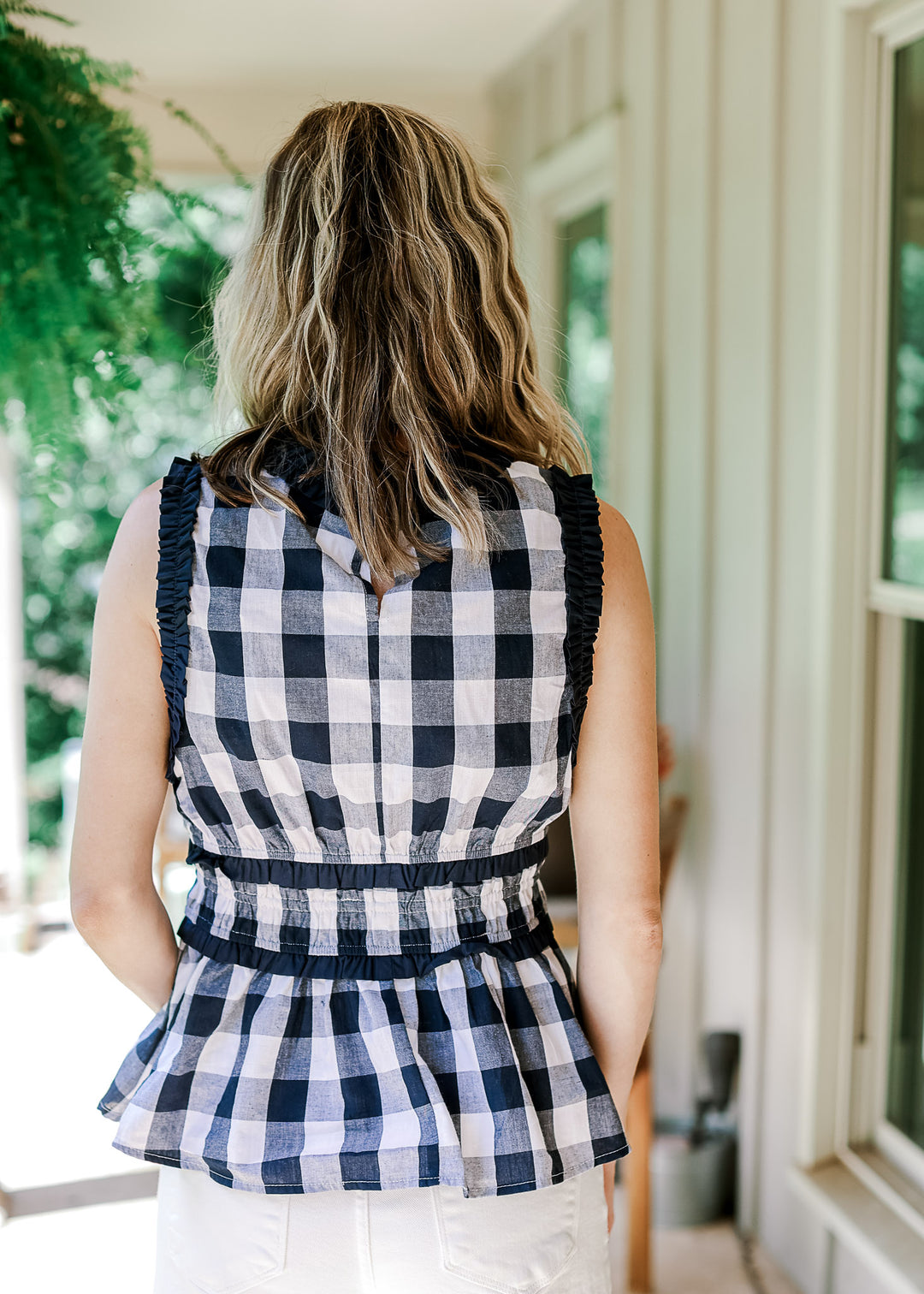 Back view of Model wearing a navy and white gingham sleeveless top with keyhole and elastic waist.