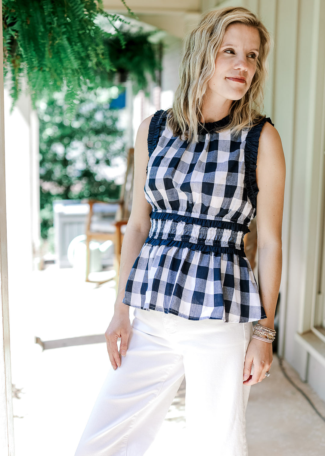 Model wearing white pants and a navy and white gingham top with a round neck and elastic waist.