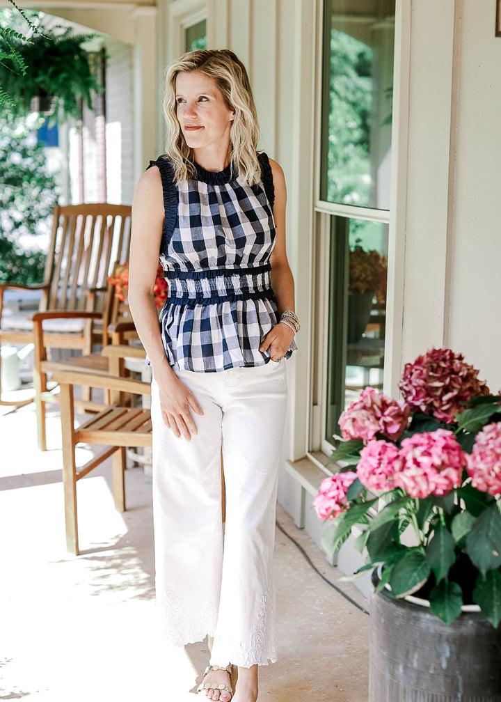 Model wearing white pants, sandals and a navy and white gingham top with an elastic waist.