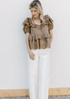 Model wearing a golden brown short sleeve top with ruffles at neck, sleeve and waist.
