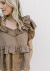 Close up of ruffles at neck, sleeve and waist on a golden brown short sleeve top with v-neck. 