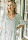 Close up of v-neck with a tie and bubble short sleeves on a sage above the knee dress.