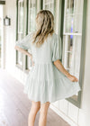 Back view of a sage above the knee dress with bubble short sleeves and a v-neck with a tie.