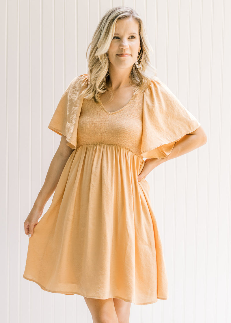 Model wearing a salmon above the knee dress with a smocked bodice and flutter short sleeves. 