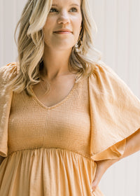 Close up view of a smocked bodice and flutter short sleeves on a salmon dress.