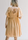 Back view of a model wearing a salmon dress with a smocked bodice, short sleeves and a tie closure. 