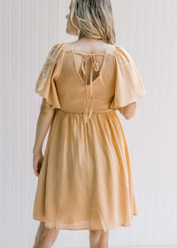 Back view of a model wearing a salmon dress with a smocked bodice, short sleeves and a tie closure. 