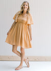 Model wearing sandals with a salmon dress, a smocked bodice and flutter short sleeves.