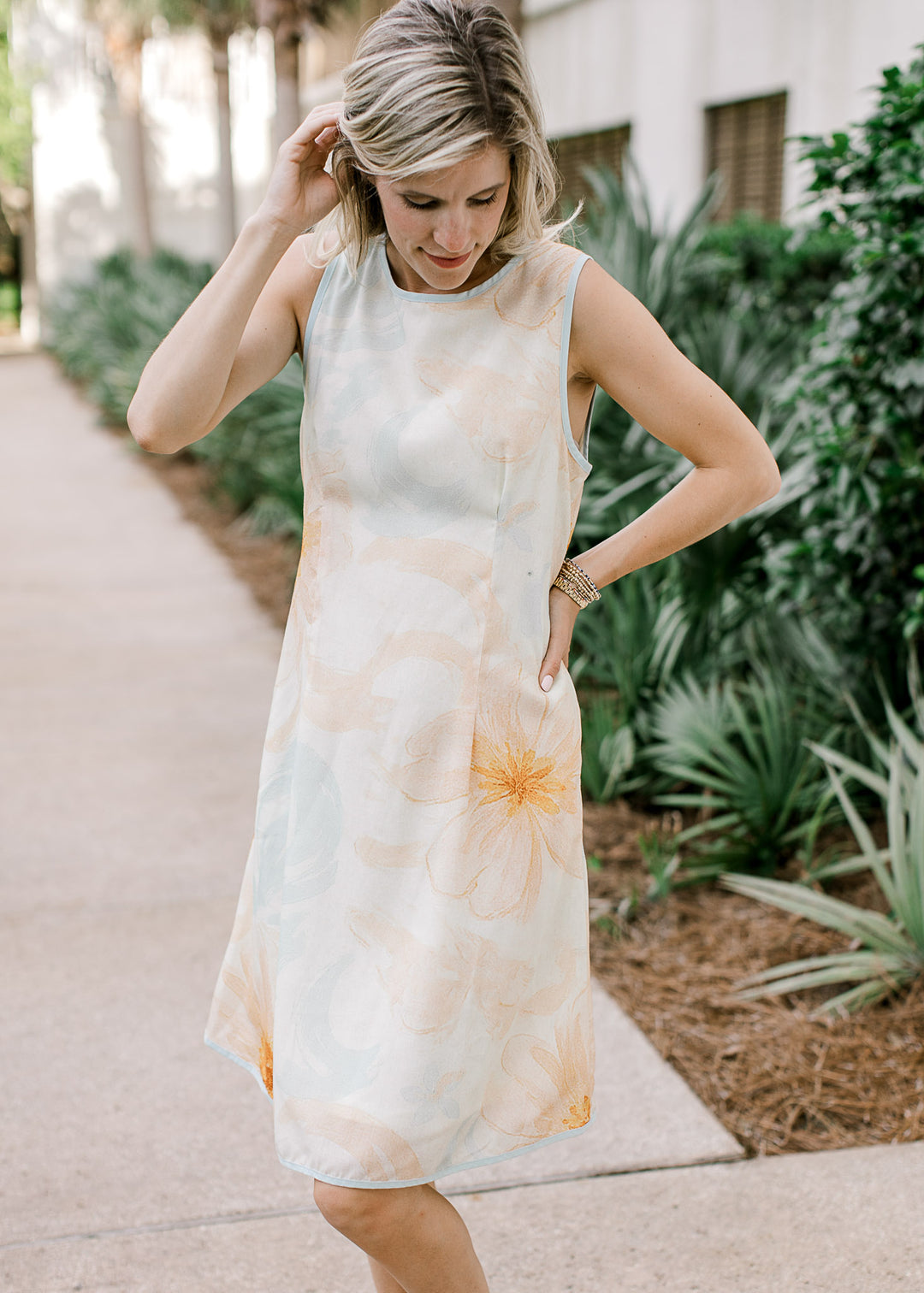 Model wearing a sleeveless cream knee length dress with orange and baby blue floral. 