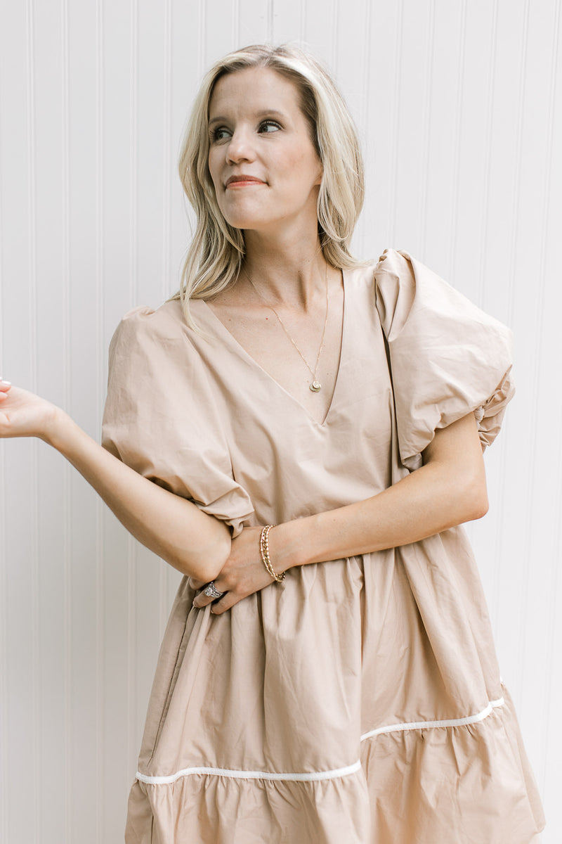 Model wearing a wheat v-neck dress with cream strip detail and short puff sleeves.