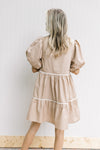 Back view of Model wearing a wheat colored dress with cream strip detail and short puff sleeves.