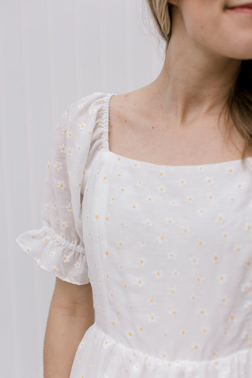 Close up of square neckline on a white top adorned white and yellow daises and short poet sleeves.