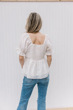 Back view of Model wearing a white top adorned white and yellow daises and a square neckline.
