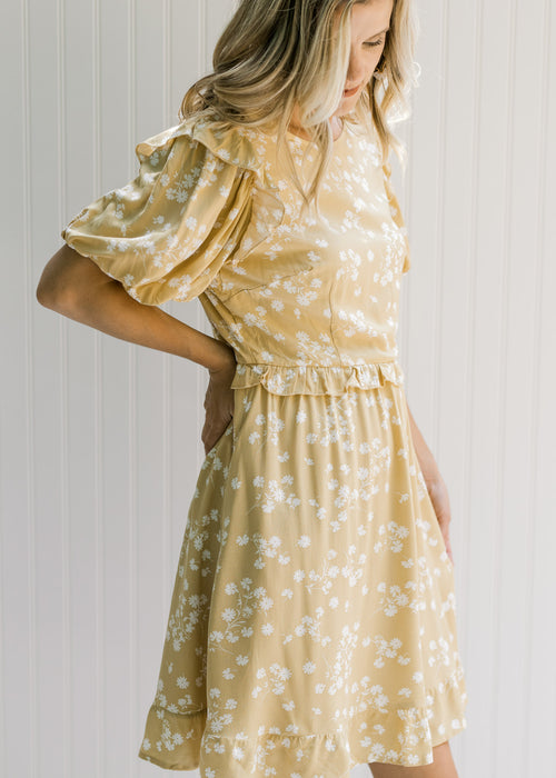 Model wearing a mustard colored dress with a cream floral pattern and short puff sleeves.