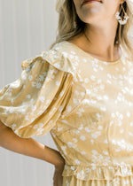 Close up view of ruffle at shoulder and waist on a yellow dress with cream floral and short sleeves.