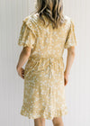 Back view of Model wearing a yellow dress with a cream floral pattern and a hidden back zipper. 