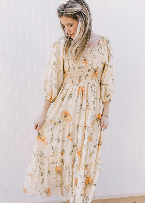 Model wearing a light yellow dress with orange and green flowers and a smocked bodice. 