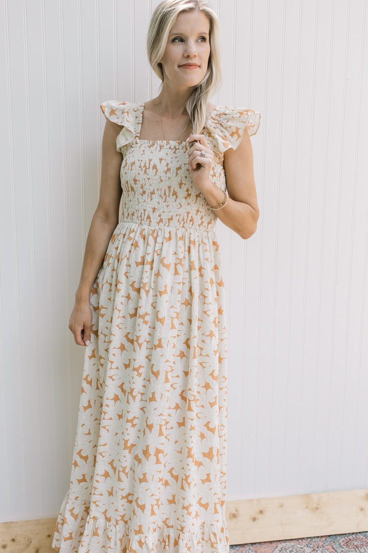 Model wearing a soft orange dress with cream flowers, square neckline and flutter cap sleeves.