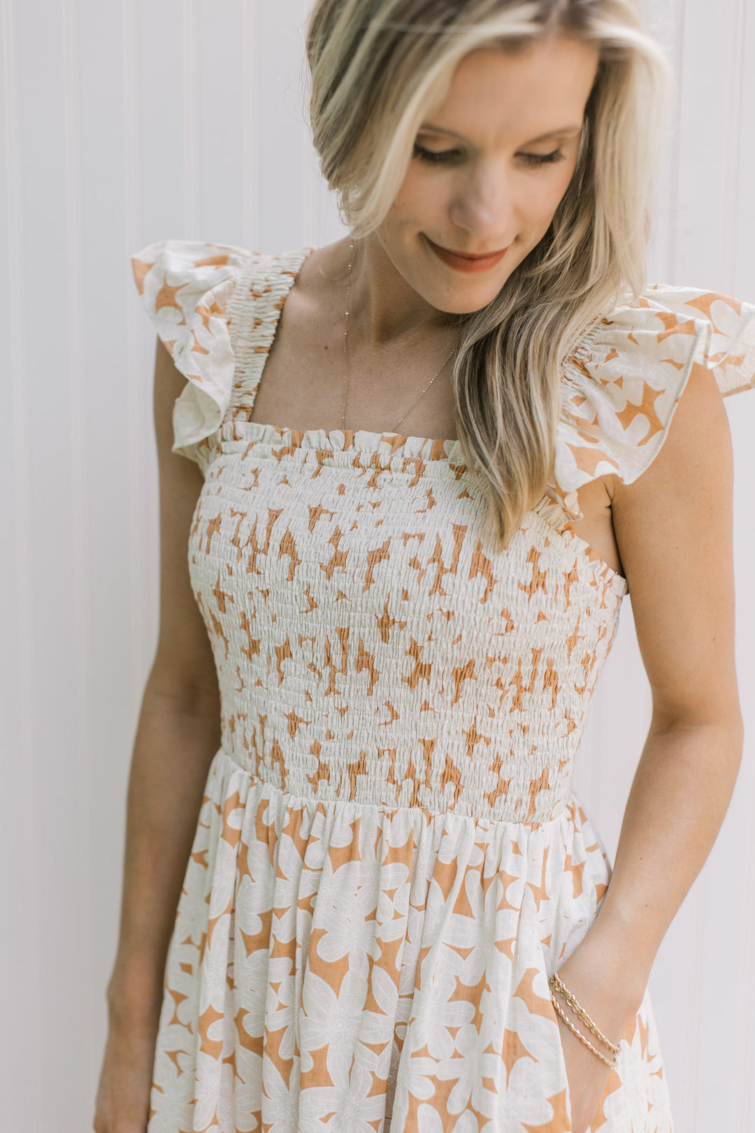 Close up of smocked bodice, square neck and flutter sleeves on an orange dress with cream flowers. 