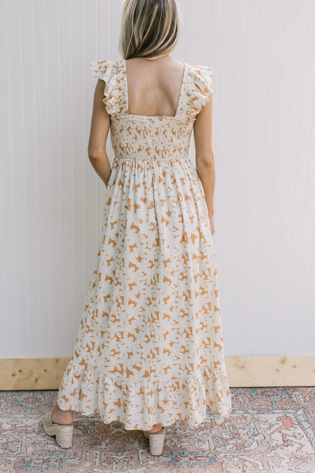 Back view of Model wearing a soft orange dress with cream flowers, smocked bodice and square neck.