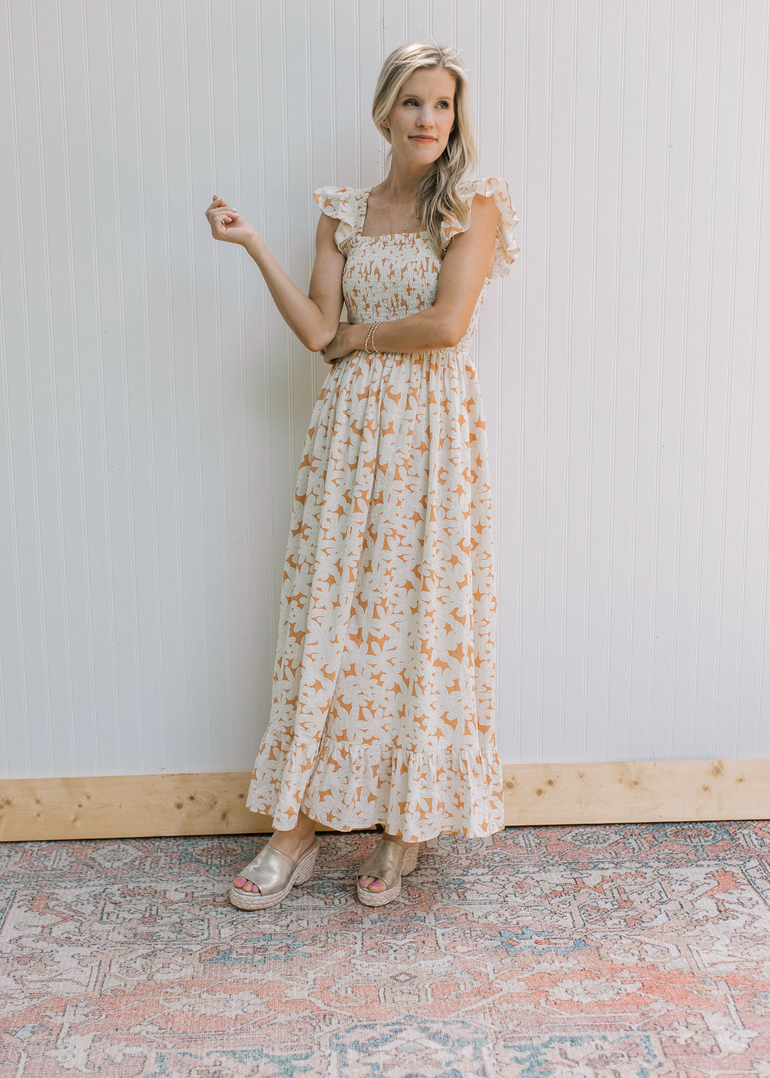 Model wearing a soft orange dress with cream flowers, smocked bodice and flutter cap sleeves. 