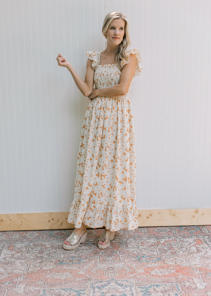 Model wearing a soft orange dress with cream flowers, smocked bodice and flutter cap sleeves. 