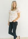 Model wearing jeans and sandals with a white and coral embroidered floral top with bubble sleeves. 
