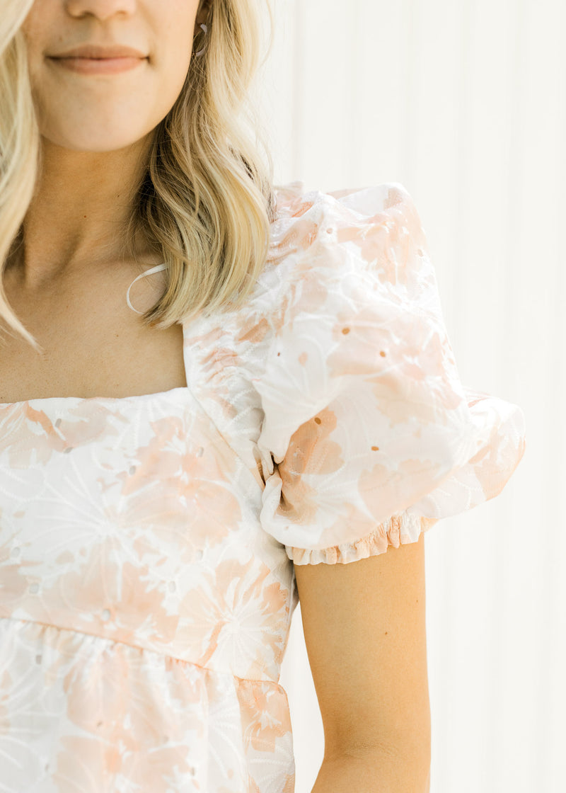 Close up view of bubble short sleeves and square neck on a white and coral embroidered floral top. 